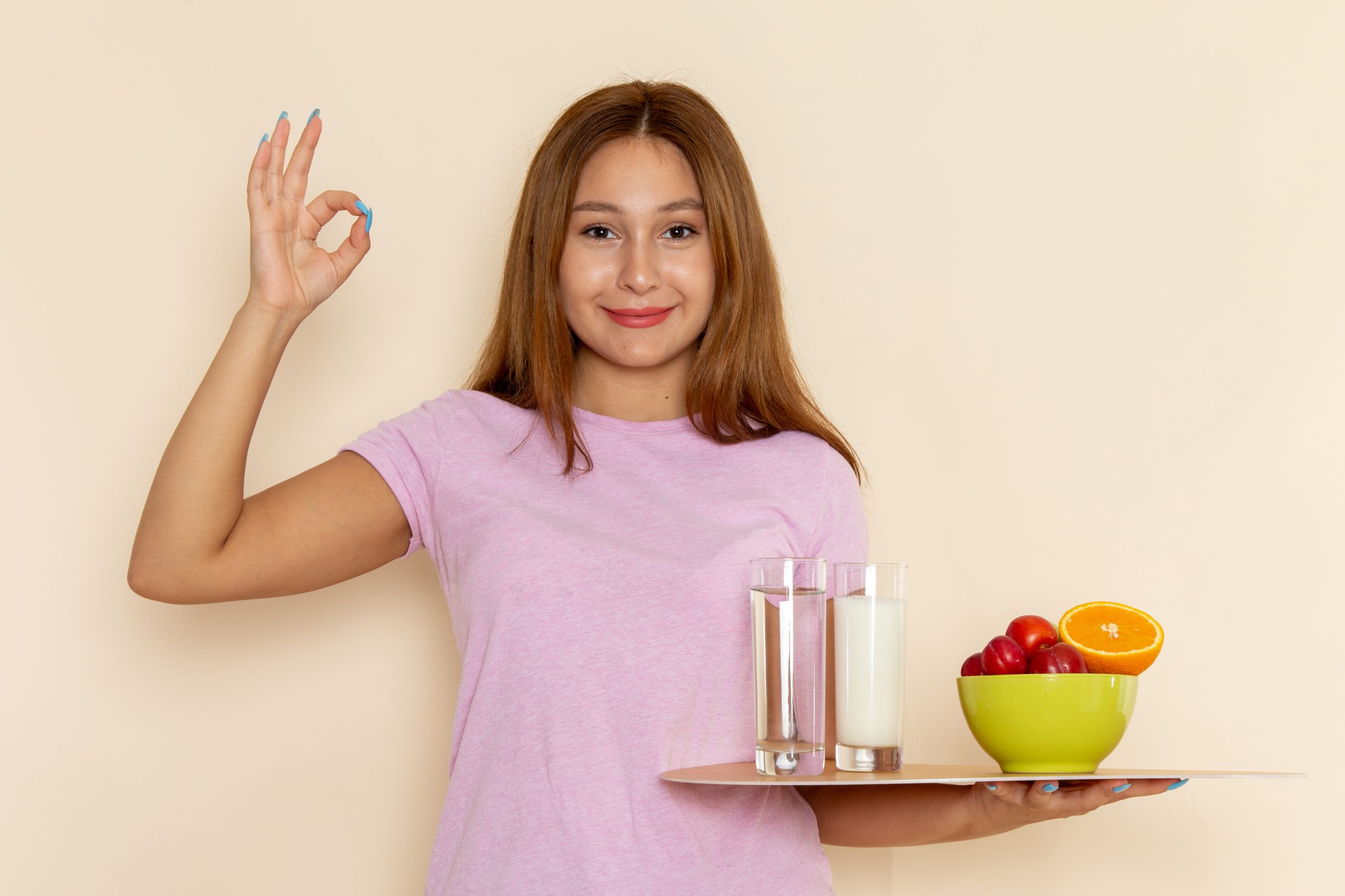 front view young female pink t shirt blue jeans holding tray fruits milk water smiling grey scaled